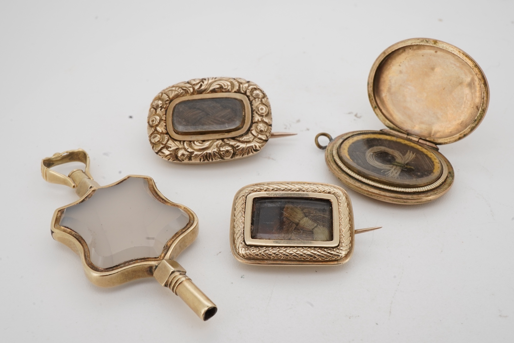 A locket, a watch key and two mourning brooches, the oval locket engraved with foliate details, opening to reveal a glazed panel of hairwork; together with two early 19th century mourning brooches, engraved with flowers